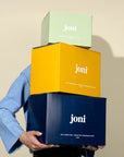 Three stacked 'joni' boxes of different colors held by a person wearing a blue sleeve.