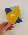 Hand holding a colorful travel period care mini box by joni, featuring bold geometric designs.