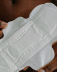 Close-up of bamboo overnight pad held by hands, designed for heavy flow with ultra-thin and ultra-absorbent features.