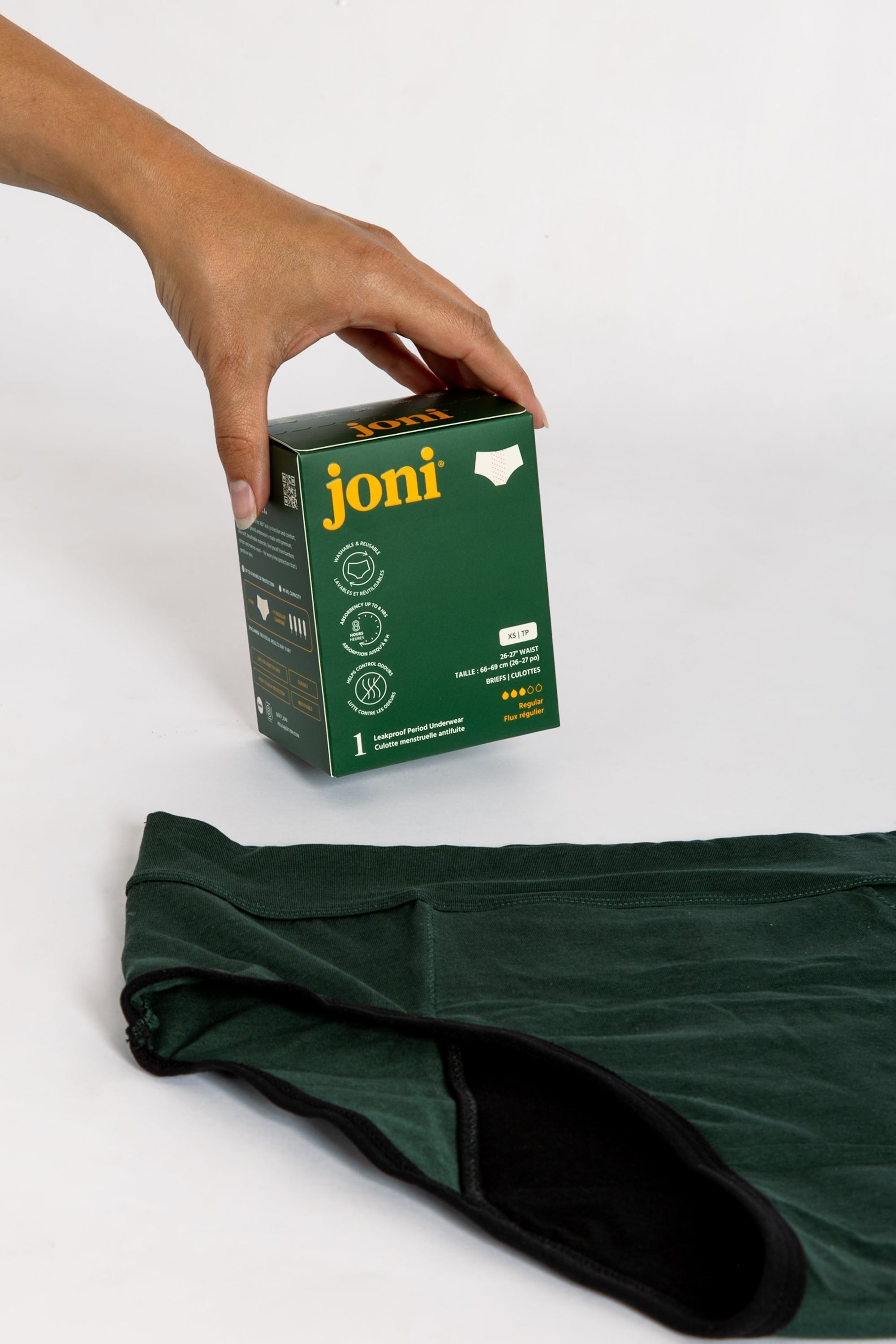 A hand holds a box of joni leakproof period underwear with a pair laying flat on a white background
