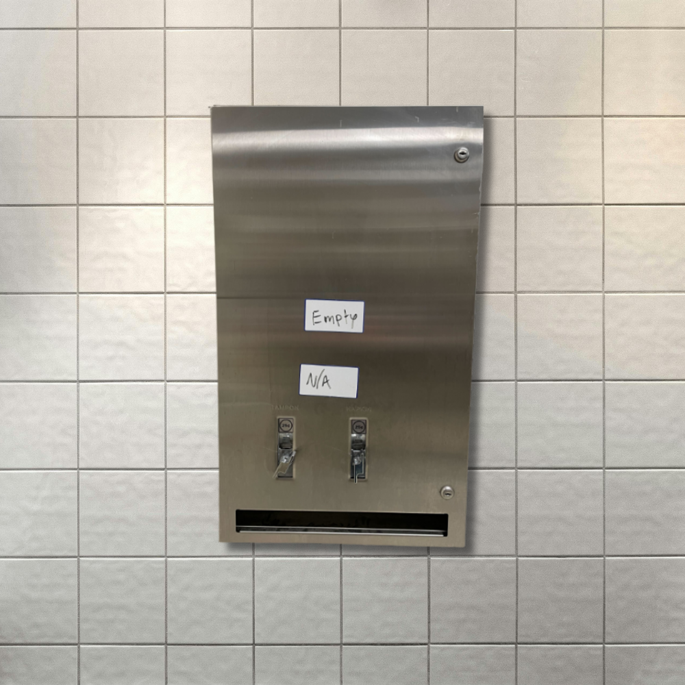 An empty period care dispenser hangs on the wall of public washroom