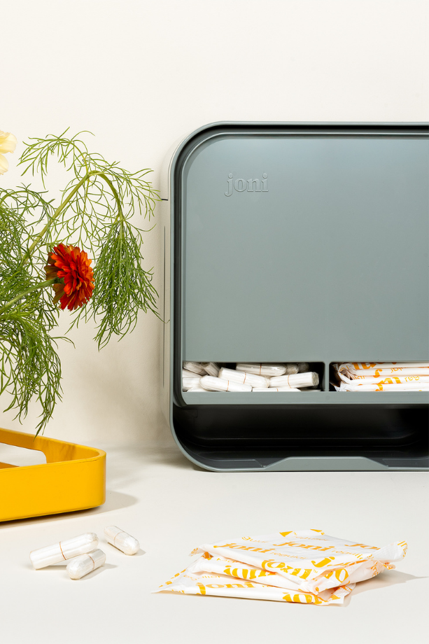 joni Model A period care dispenser on a washroom countertop with a plant
