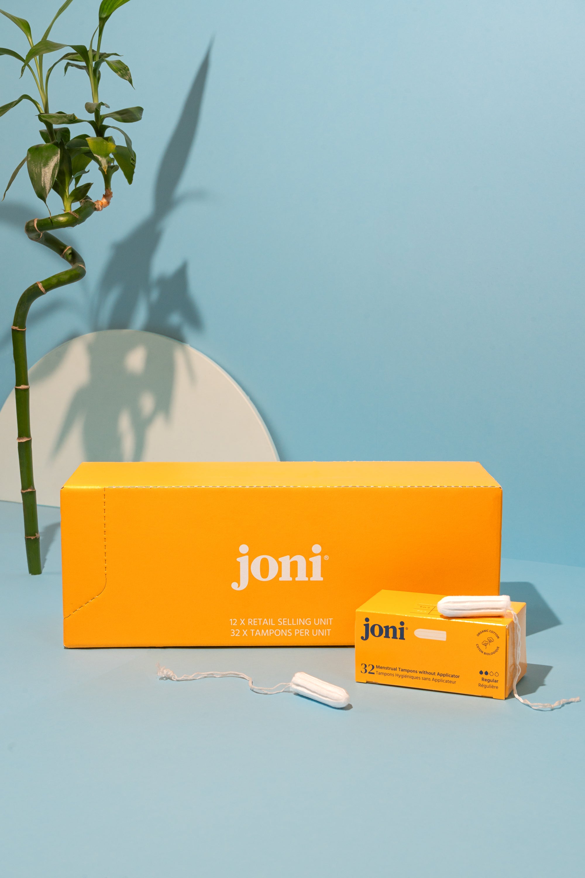 Yellow casepack of joni regular tampons for commercial washrooms with a blue background and bamboo  